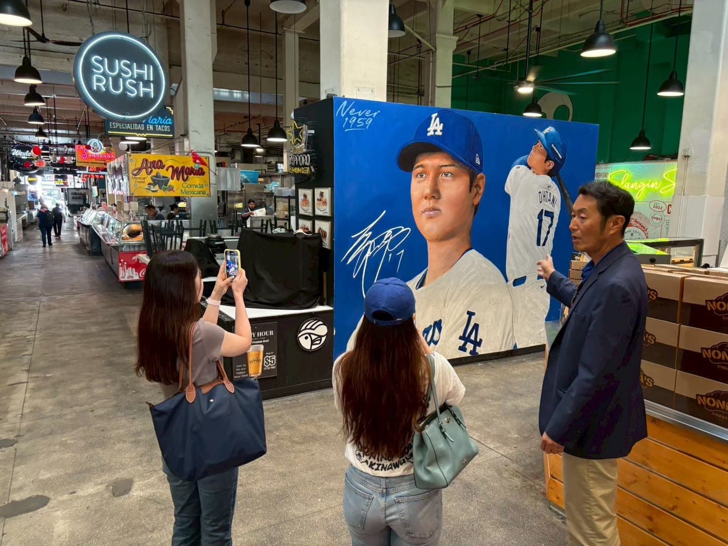Guide Imai explaining to guests in front of a Shohei Ohtani mural.